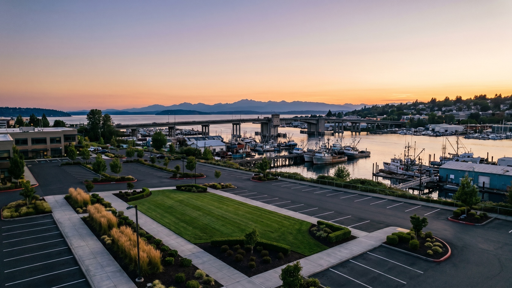 Aerial view of a manicured commercial property above Salmon Bay with the Ballard Bridge, fishing fleet, and Olympic Mountains at golden hour